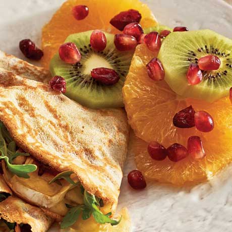 A turkey, brie and cranberry stuffed crepe on a white plate served alongside an orange and kiwi fruit salad.