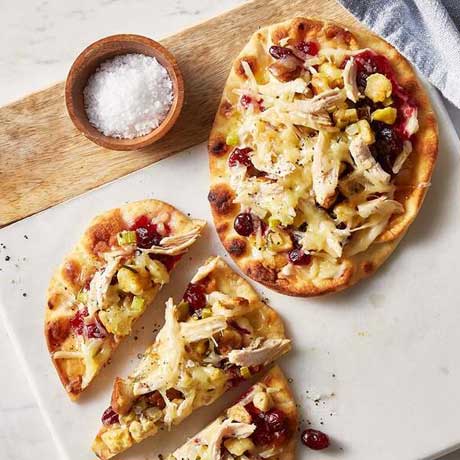 Naan topped with shredded leftover turkey meat, cranberry sauce, and cheese on a white marble board.