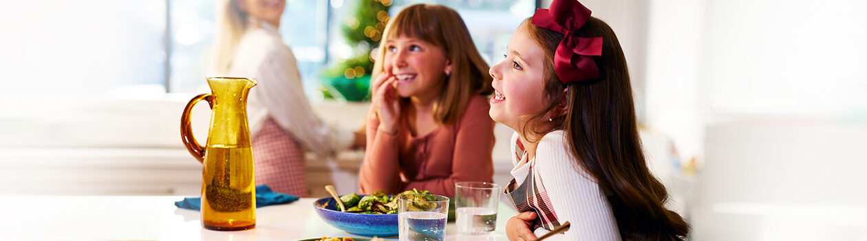 Two smiling little girls sitting at a marble island countertop with dishes full of food in front of them.