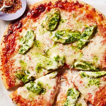 Top down shot of a cheese pizza with dollops of pesto
