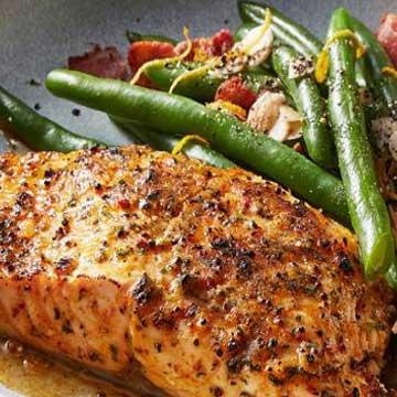 A marinated salmon fillet in a grey bowl next to a side of green beans flecked with almonds and lemon zest.