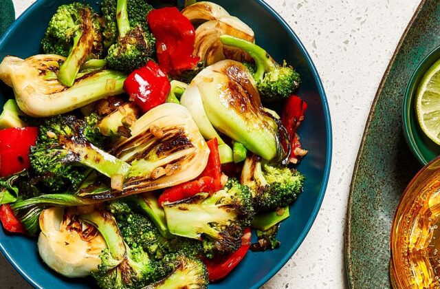 Charred bok choy and broccoli in a blue bowl on a white countertop.