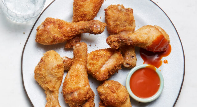 Light blue plate of chicken wing drumsticks with a side of hot sauce.