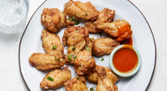 Light blue plate with chicken wings and hot sauce on it