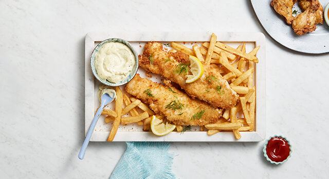 White rectangular plate full of fish and chips with a side of tartar sauce.