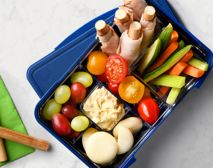 Blue bento box with each compartment filled with breadsticks wrapped with turkey deli slices, cheeses, dip and veggies.