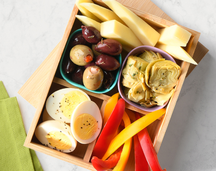 Wooden bento box featuring vegetarian options including olives, cheese, marinated artichokes, bell pepper slices and hard-boiled eggs.