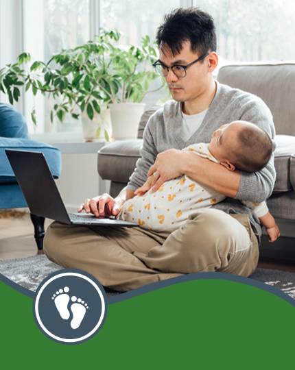 Parent holding baby while typing on a laptop