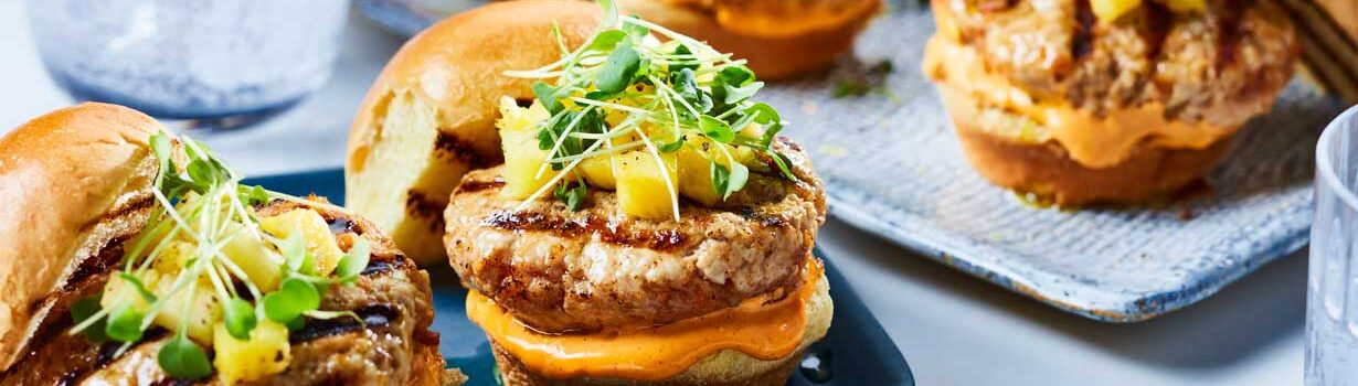 Korean-style pork sliders topped with pineapple cubes and micro greens on a blue plate.