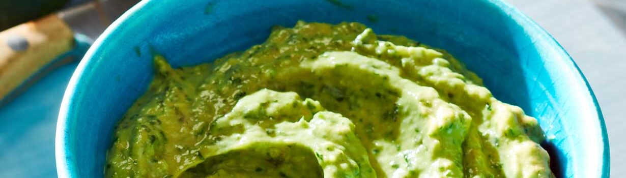 Blue bowl filled with a light green avocado tahini herb sauce.