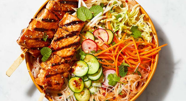 Orange plate topped with Teriyaki salmon skewer rice noodle salad.