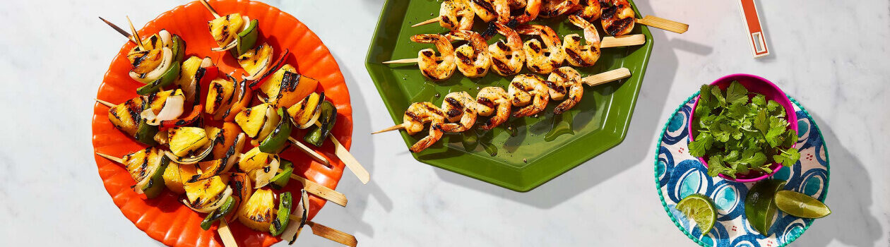 Shrimp kabobs and pineapple & Pepper kabobs on an orange plate on a white countertop.