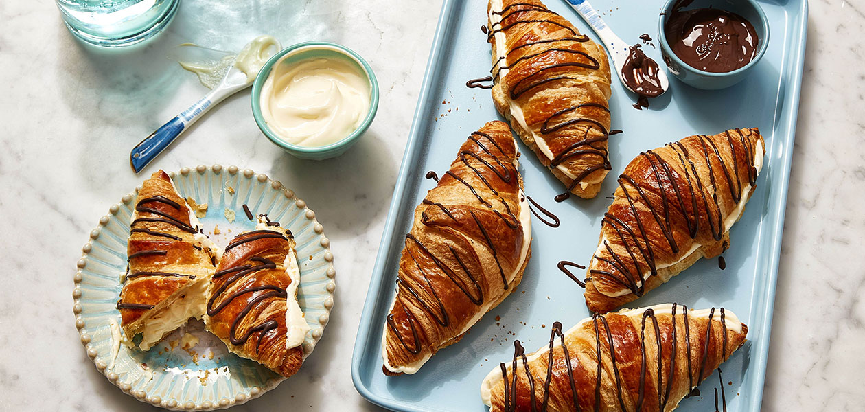 Boston cream croissants on a rectangular light blue serving platter next to a single croissant on a blue plate.