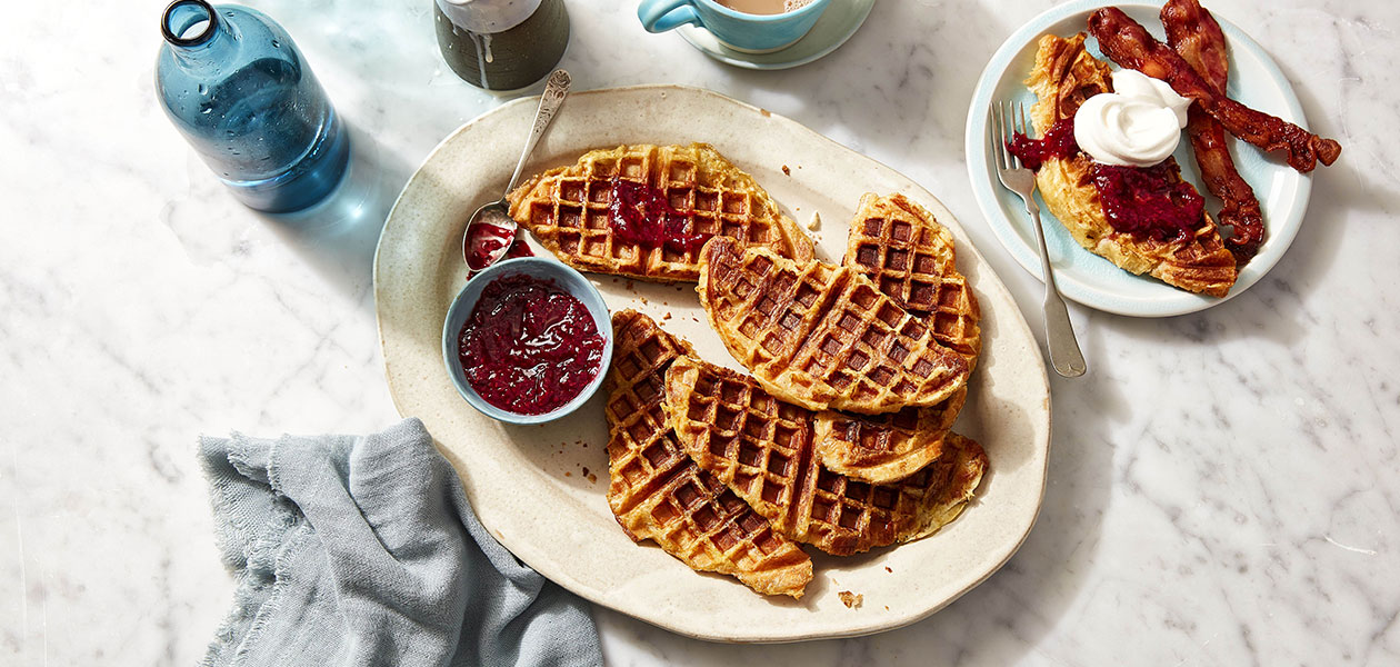 Three serving platters: one filled with waffle croissants, another with a croissant topped double cheese and ham strata and one with almond filled croissants.