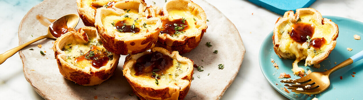 Mini French onion quiches made with hamburger buns on a beige plate next to a little bowl of chutney.