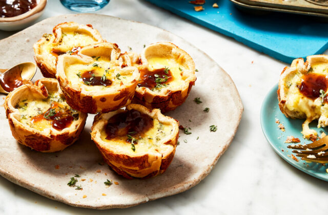 Mini French onion quiches made with hamburger buns on a beige plate next to a little bowl of chutney.