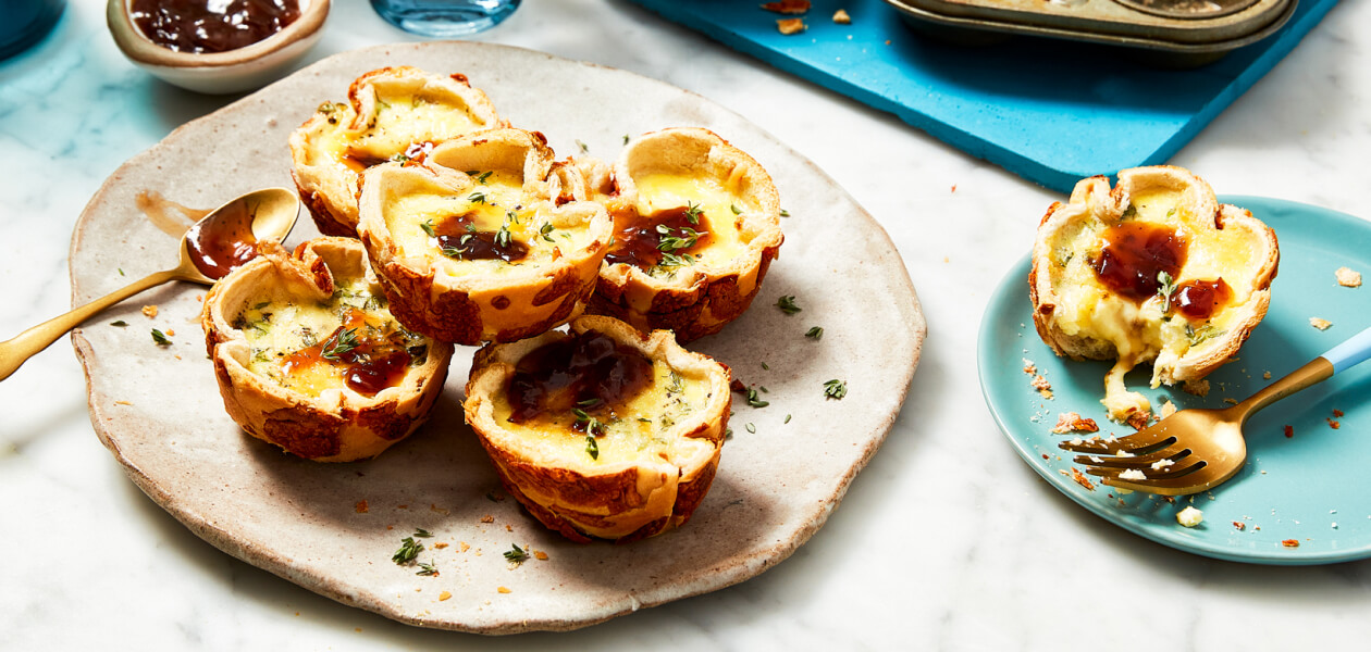 Mini French onion quiches made with hamburger buns on a beige plate next to a little bowl of chutney.