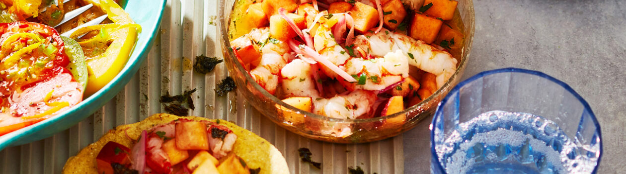 Bowl of grilled shrimp and peach ceviche next to a tostada with a topped tortilla.