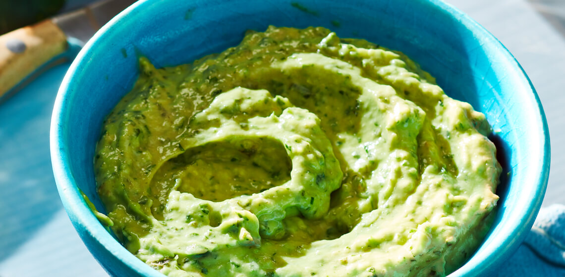 Blue bowl filled with a light green avocado tahini herb sauce.