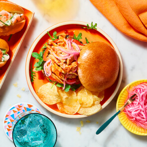 Orange round plate topped with a BBQ pulled Portuguese-style chicken sandwich.