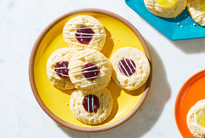 Round thumbprint-style cookies with blueberry pie filling sitting on a bright yellow plate.