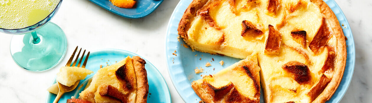 Brioche pudding pie in a pale blue pie plate next to a serving on a blue plate with fresh fruit.