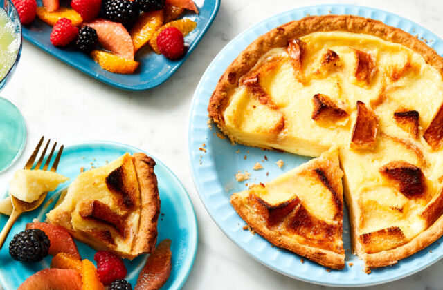 Brioche pudding pie in a pale blue pie plate next to a serving on a blue plate with fresh fruit.