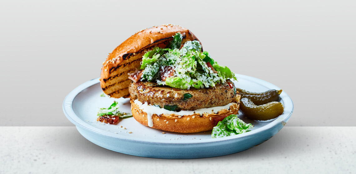 Turkey Kale Burger topped with Ceasar salad and all of the fixings on a blue plate.