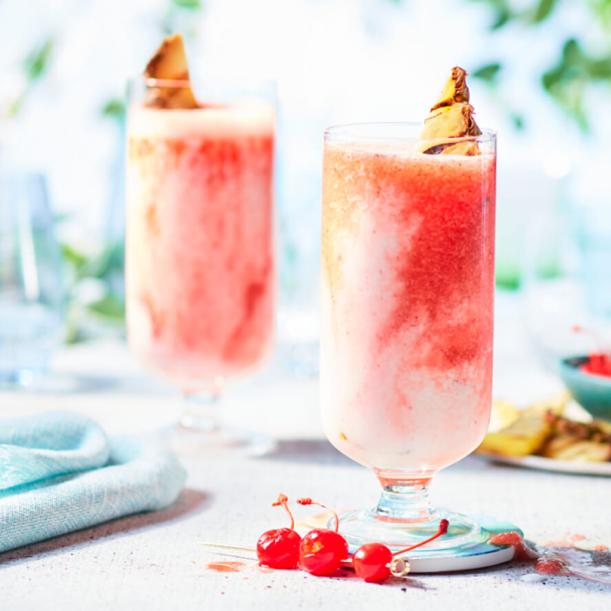 Tall glasses full of the icy pink and white Cherry Miami Vice Cocktail on a grey countertop with turquoise napkins off to the side.