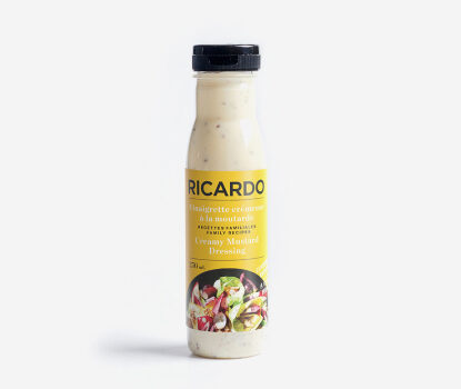 Clear glass bottle of Creamy Mustard Dressing with mustard yellow label depicting a salad with dressing on top.