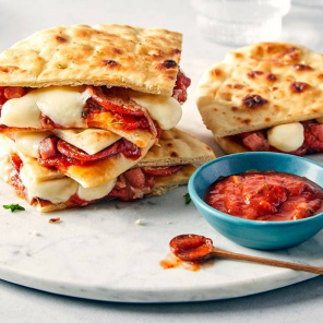 Baked flatbread pizza sandwich filled with pancetta, cheese and tomato sauce sitting atop a white marble countertop.