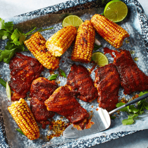 Paprika grilled chicken thighs and corn on a black and white speckled serving tray next to glasses of sparkling water.