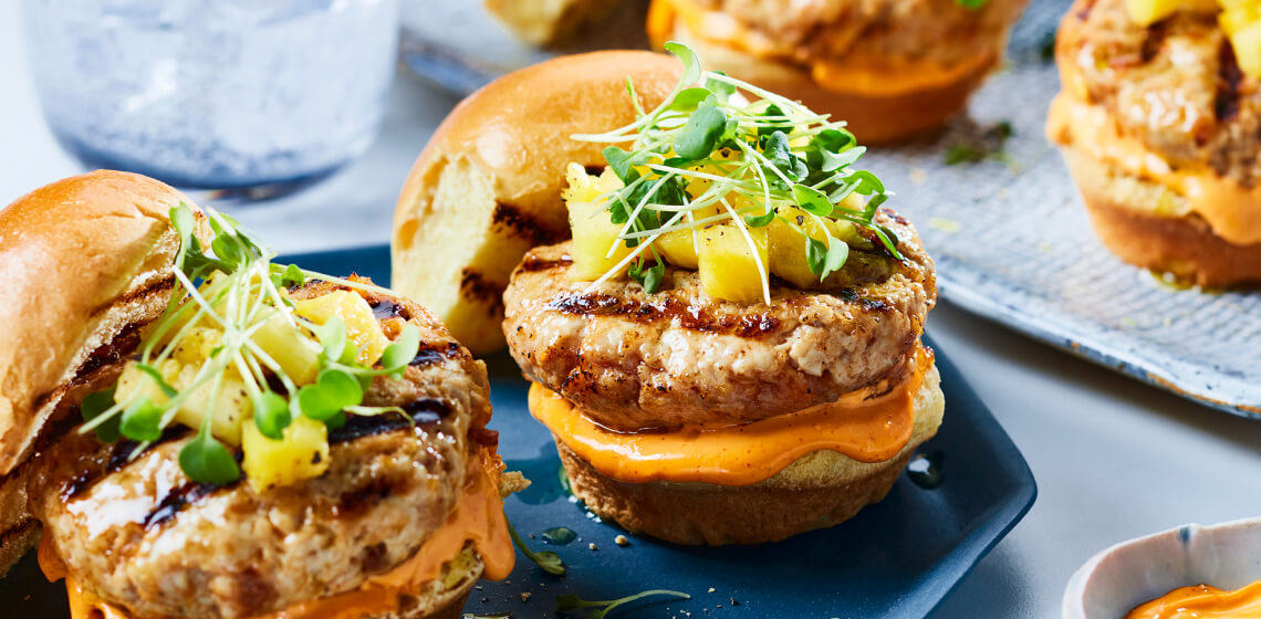 Korean-style pork sliders topped with pineapple cubes and micro greens on a blue plate.