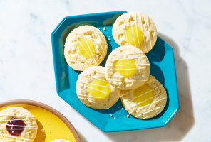 Round thumbprint-style cookies with lemon pie filling sitting on a turquoise plate.