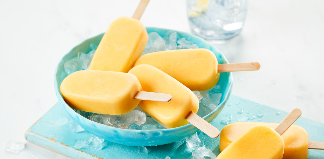 Several golden milk smoothie pops in a light blue bowl sitting a top ice.