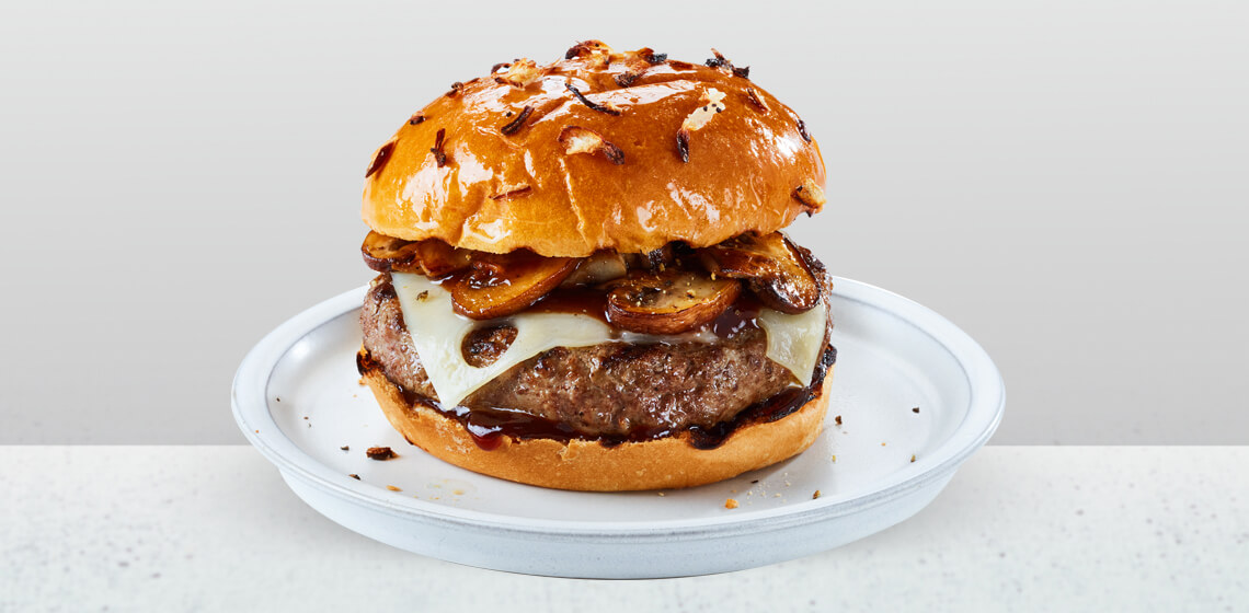 Mushroom and Swiss Cheeseburger with sauteed onions on an onion bun sitting on a white countertop.