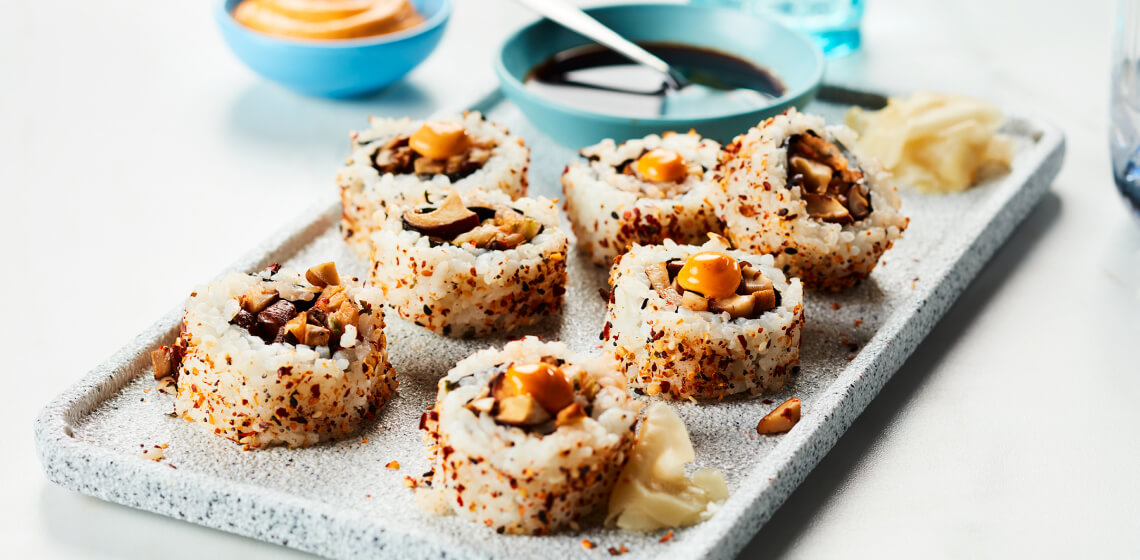 Several mushroom rolls sitting on a gray serving platter next to a little blue bowl of soy sauce.