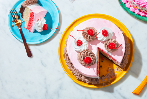 Triple-layer Neapolitan cake iced in white and pink with a chocolate border, sitting atop a blue dessert plate with a fork next to it.