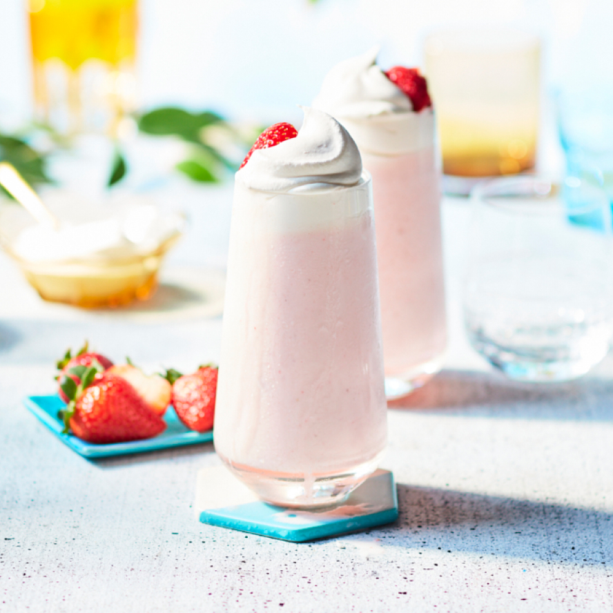 Tall, thin glasses filled with a Pink Whippet Strawberry Lemonade frosted beverage in swirls of pink and white topped with a strawberry and whipped cream.