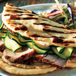 Pork sandwich with quick zucchini pickles close up on a white plate with a pile of slaw next to it.