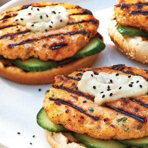 Mayo-and-sesame-topped salmon burgers on buns served on a white plate.