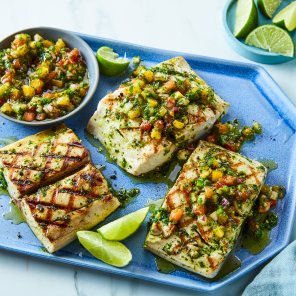 Mahi Mahi filets with a summer herb sauce and heirloom tomato salsa on a periwinkle plate with lime segments scattered on platter.