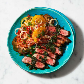 Turquoise plate topped with slices of Sterling Silver Striploin grilling steak topped with summer herb sauce and next to an heirloom tomato salad.
