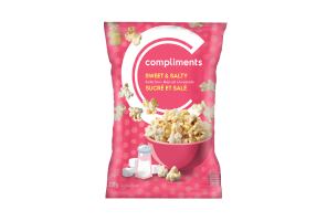 A pink packet of Compliments Sweet & Salty Kettle Corn, featuring an illustration of a salt shaker and sugar cubes on the front of the pack, along with a pink bowl of the popcorn.