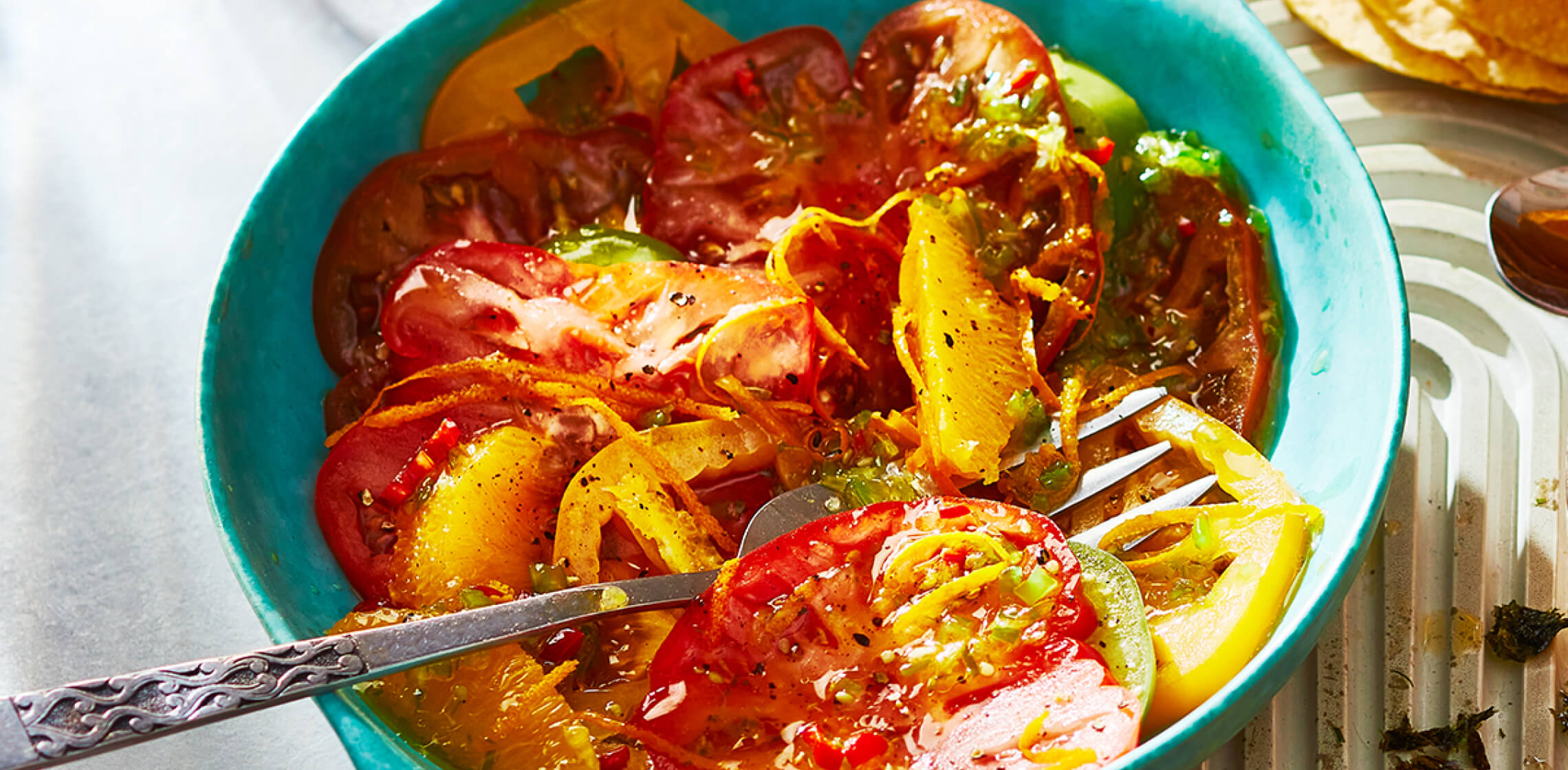 Blue bowl filled with Heirloom Tomato Ceviche-Style Salad with serving spoons.