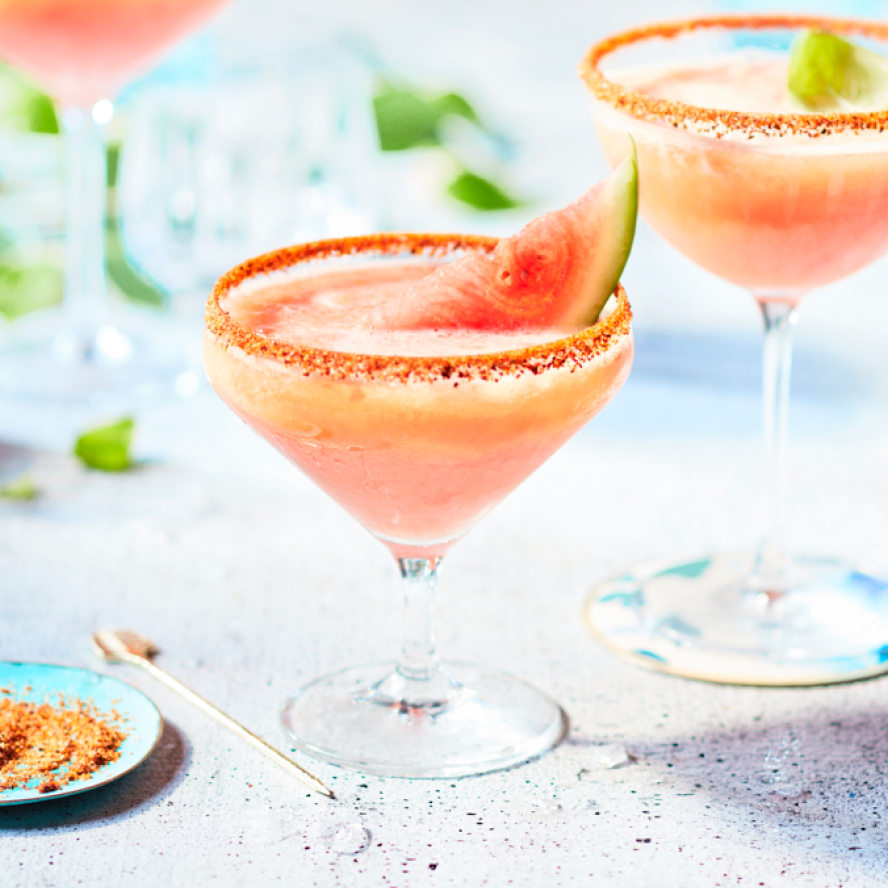 Salt-rimmed margarita glasses filled with a pink slushy version of a watermelon beergarita garnished with a small wedge of watermelon.