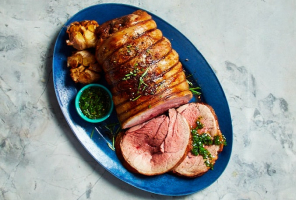 Top-down view of a place setting with circular dish of lamb and roasted garlic on a blue plate.