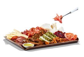 Deli meat on a silver fork above a charcuterie board with various meats, cheese, and almonds.