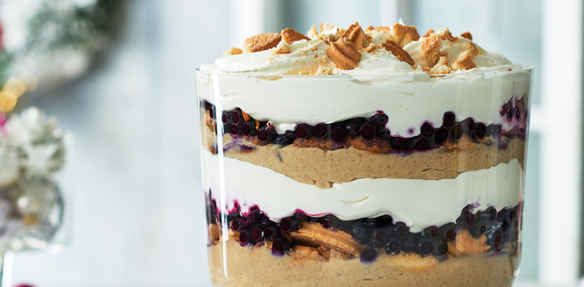 A layered trifle of gingerbread-flavoured custard, crumbled butter cookies, and thawed honey-sweetened blueberries with clouds of whipped cream between and on top. 