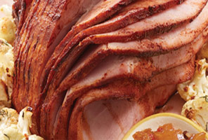 sliced ham on pink plate with small bowl of pineapple chutney surrounded by vegetables.